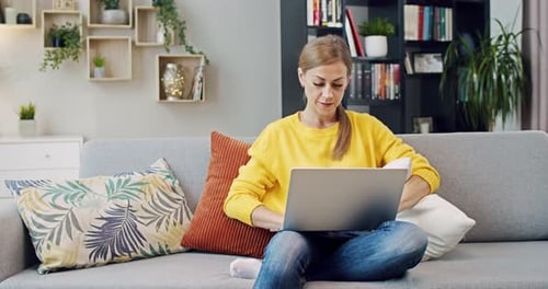 Woman Using Laptop on Sofa in Home