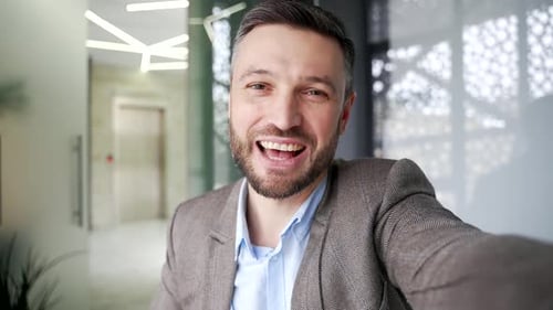 POV. A smiling businessman talking on a video call using a phone in a business office. Happy