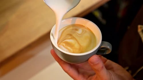 Barista pouring milk into coffee for latte art. Making fresh cappuccino in a cafe. Close up view.