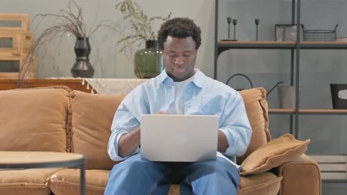 Young Adult Using Laptop on Sofa at Home