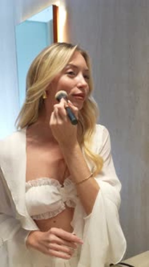 Woman Applies Makeup with Brush in Bathroom Setting