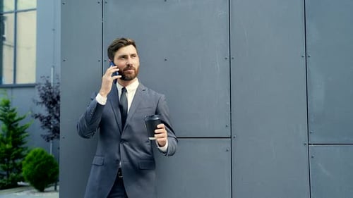 Bärtiger Geschäftsmann im formellen Anzug in der Pause mit Handy und Smartphone. Geschäftsmann stehend