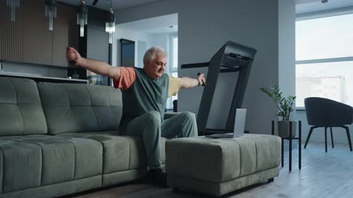 Senior Man Doing Physical Exercise With Dumbbells At Home Watching Online Video Training At Laptop