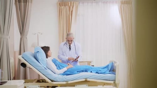 Caucasian senior doctor checking up female patient in hospital ward.
