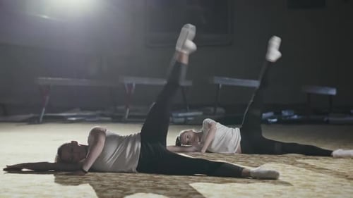 Junge flexible Turnerinnen liegen auf dem Boden und machen während des Trainings synchron Übungen
