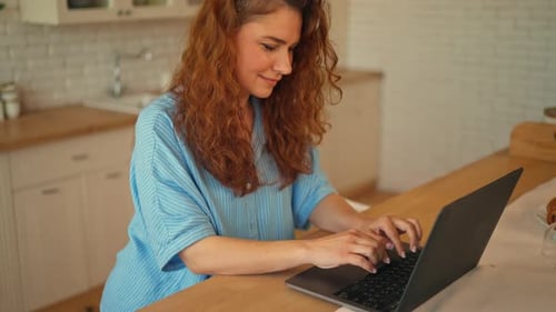 Woman Typing on Laptop in a Bright Kitchen