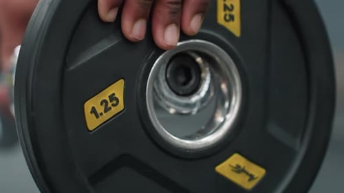Close Up Barbell Plate Being Loaded with 125 Weight in Fitness Gym Setting