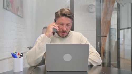Man Working on Laptop and Talking on Phone