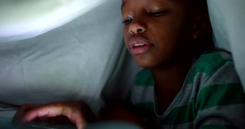 Enfant africain utilisant un smartphone la nuit sous une couverture, enfant métisse utilisant la technologie