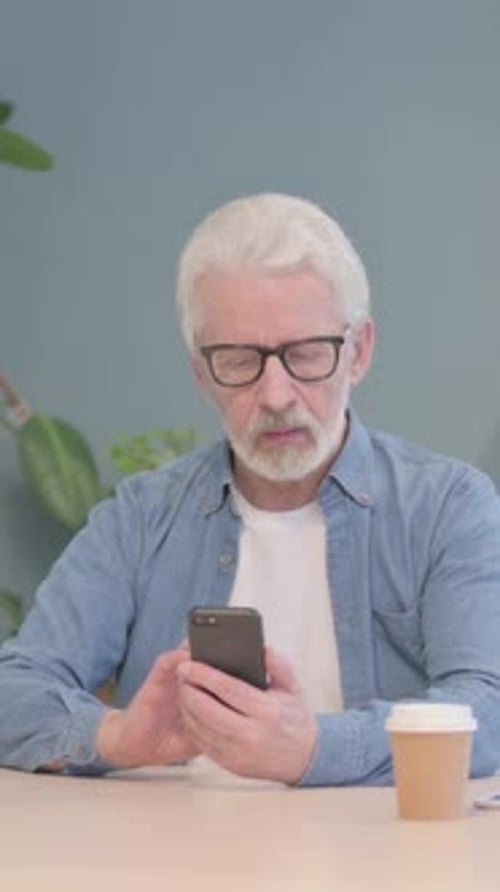Senior Man Using Smartphone While Sitting at Table