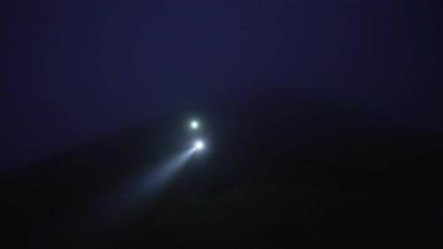 Person Hiking in Dark Mountains With Headlamp