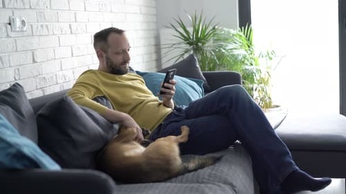 Man on couch uses phone with dog