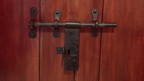 Close-up of a rustic, metal latch on a wooden door with natural lighting