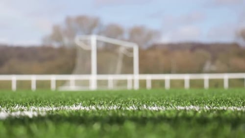 Niedriger Schuss, der den Fokus vom Gras auf einem Fußballfeld bis zu einem Fußballtornetz zieht, das im Wind weht.
St