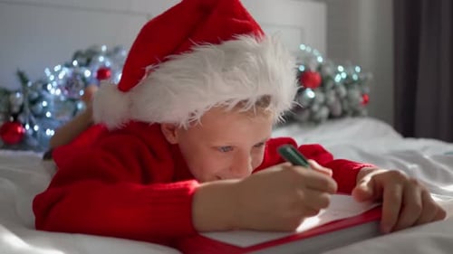 Child Writes Christmas List on Bed at Home