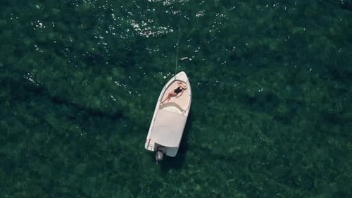Vue aérienne d'une jeune femme se relaxant et prenant un bain de soleil sur un bateau garé au milieu de l'océan.