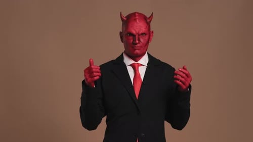 Empresario con maquillaje de diablo rojo gesticulando sobre fondo marrón