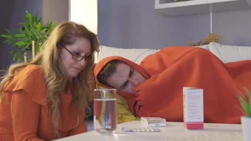Woman Caring For Sick Man Lying on Couch