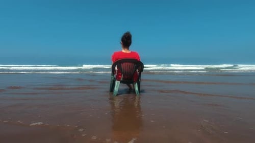 Girl sitting on a plastic chair on the Casablanca beach in Morocco and enjoying the waves. Filmed fr