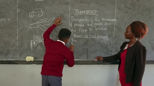 Boy And His Teacher Writing On Blackboard In African School - Medium Shot