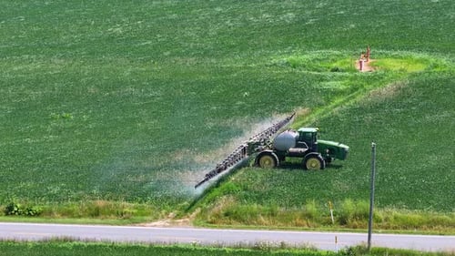 Agricultural Sprayer Tractor Spreading Chemical Pesticide Fertilizer on Growing Crops on Farm Field