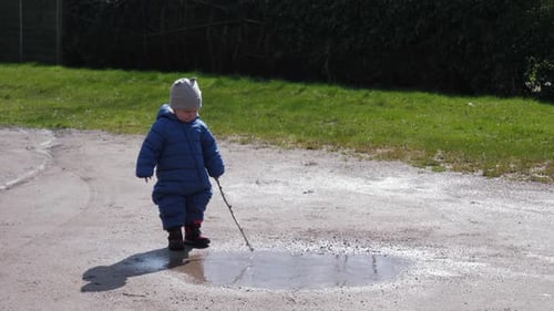 Child Playing with Stick in Puddle