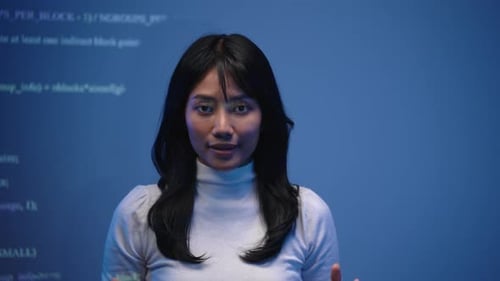 Asian woman tech speaker in a white turtleneck sweater explaining programming code