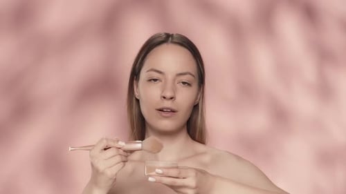 Make-up-Prozess Eine Frau taucht einen Make-up-Pinsel in ein Glas Puderrouge und trägt Kosmetik auf sie auf