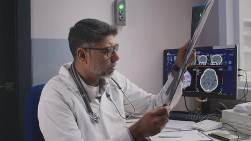 Male GP Sitting at Table in Hospital Examining MRI Film Scan