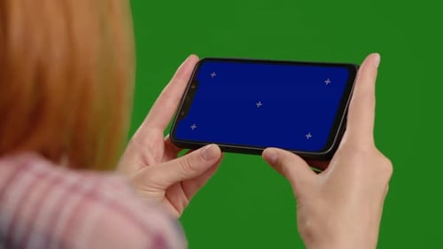 Female testing new application on blue screen horizontal phone in a green background.