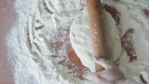 The baker rolls out the dough with a wooden rolling pin and begins to make bread.