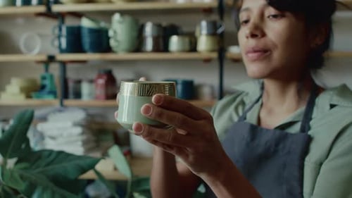 Selective Focus of Young Female Potter Examining Ceramic Green Cup