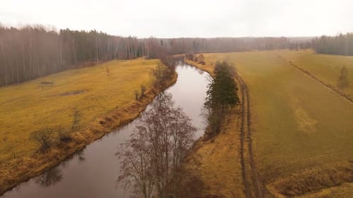Luftaufnahme eines gewundenen Flusses durch herbstliche Felder und Wälder unter bewölktem Himmel, mit sichtbarem