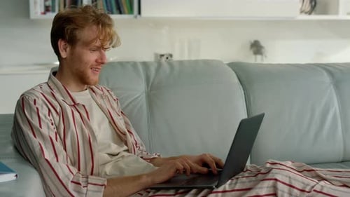 Happy ginger man waving hello talking laptop on virtual meeting in home office