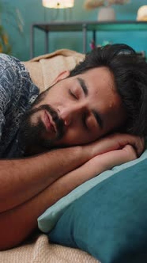 Tired Indian Man Lying Down in Bed Taking a Rest at Home Napping Falling Asleep on Sofa Relaxing