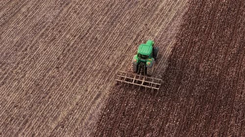 Aerial View Tractor Plowing Agricultural Field with Soil Cultivation Lines Running Farming Machinery