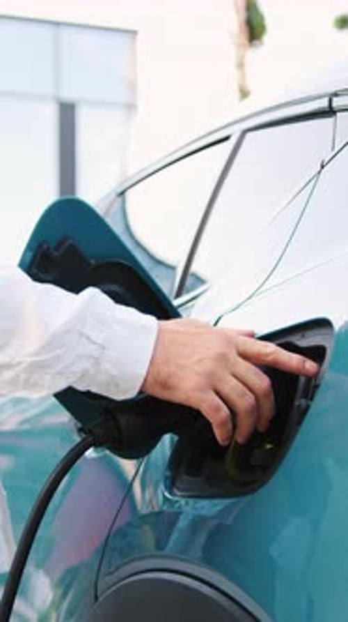 Man Removing EV Charging Cable From Electric Car After Complete Battery Charging Outdoors Slow