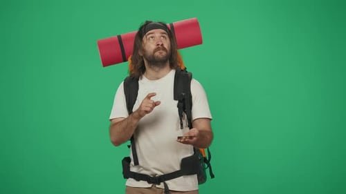 Man Tourist with Backpack Holding a Compass and Looking for Direction Where to Go Isolated on Green