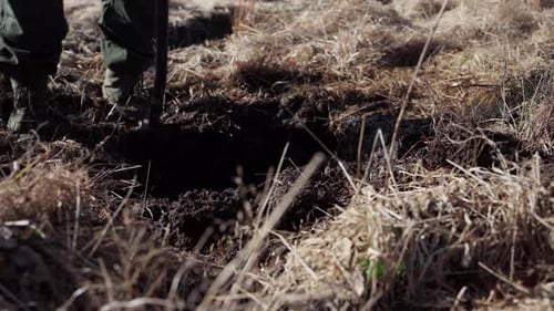 Farmer In Boots Digging Soil On Grassy Field With Shovel. closeup