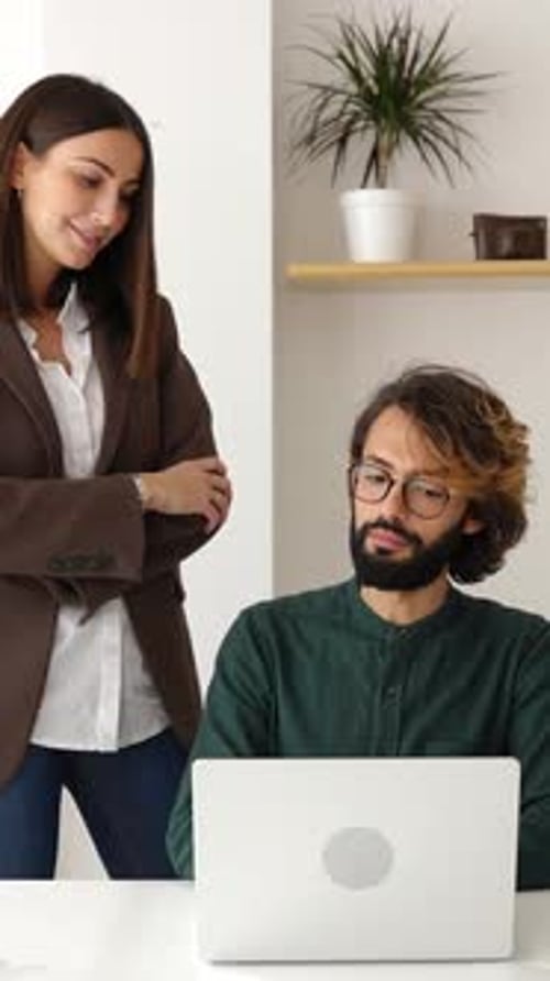 Coworkers collaborate at desk using laptop