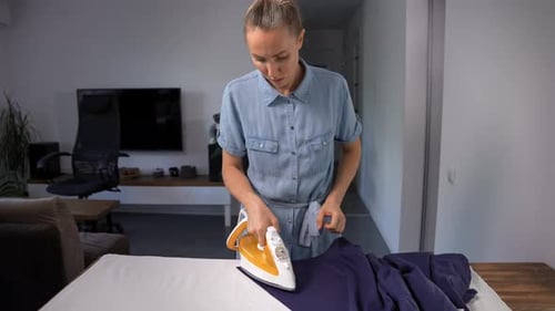 Woman ironing blue garment on ironing board at home