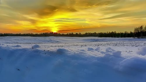 Golden sunset over a forest and snowy field - pullback sliding motion time lapse