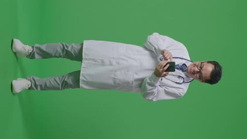 Full Body Of Asian Male Doctor With Stethoscope Using Smartphone While Standing On Green Screen