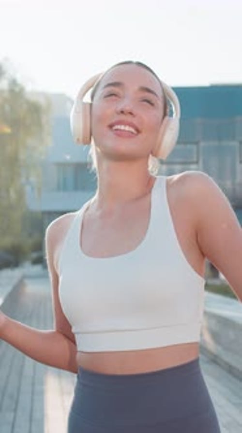 Happy Young Woman Jogger Listening to Music Via Headphones and Smartphone Walking in City Park