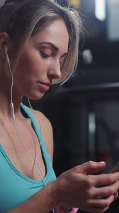 A Focused Woman in a Gym Setting Can Be Seen Wearing Earbuds While Exercising and Training