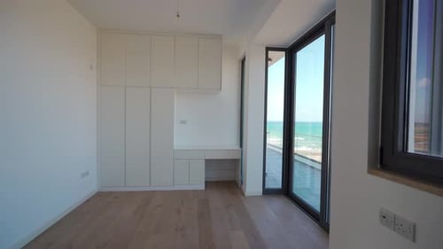 El recorrido por el ático frente a la playa muestra una habitación vacía con vista al mar, pisos de madera de diseño moderno y mucha luz