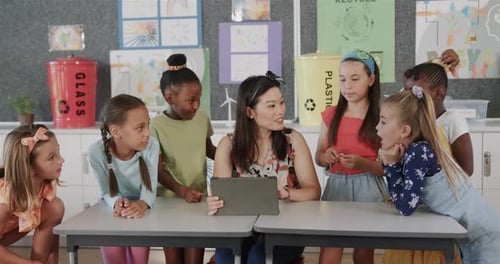 Happy diverse female teacher and schoolgirls using tablet in elementary school class, slow motion