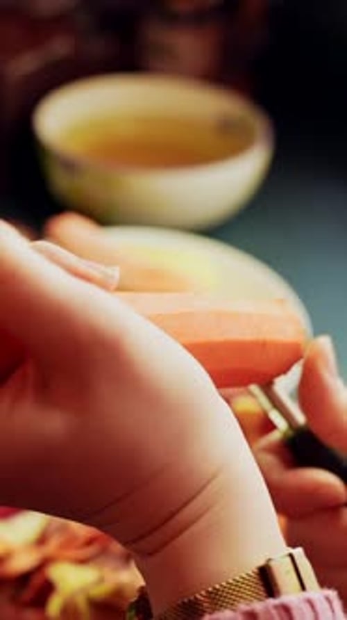 Close-up hands trim the carrot top with a vegetable peeler, removing the stem end during meal prep