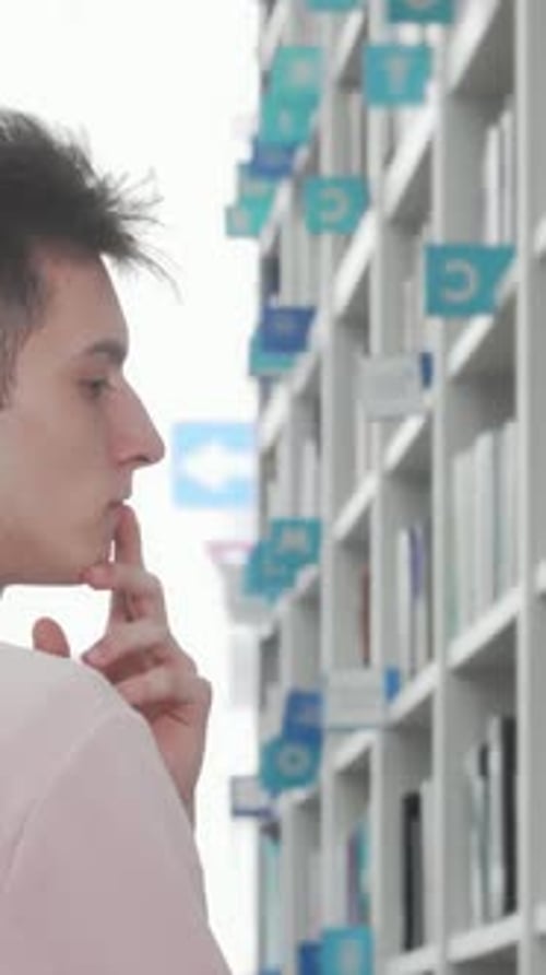 Thoughtful Young Man Exploring Bookshelves in a Bright Library