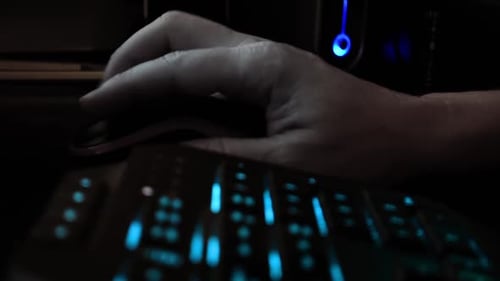 Close up on the hand of a hacker using a computer mouse, dark office